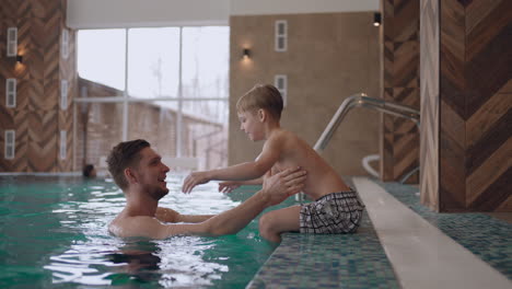 father-is-teaching-son-to-swim-in-swimming-pool-of-modern-wellness-spa-healthy-lifestyle